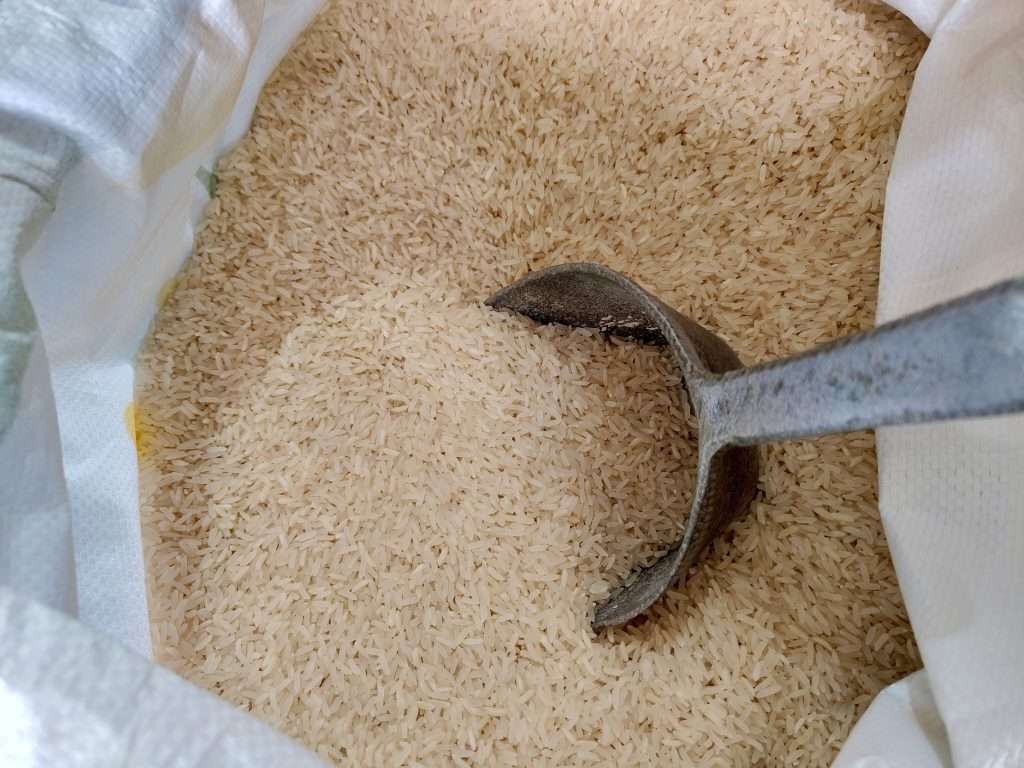 Raw rice in a white sack with a metal scoop